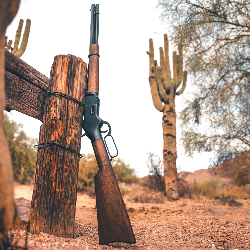 Barra 1866 Lever Action CO2 Air Rifle 3 The Barra 1866 Lever Action CO2 Air Rifle is shown leaning against a wooden post in a desert setting with cacti and dry vegetation around it.