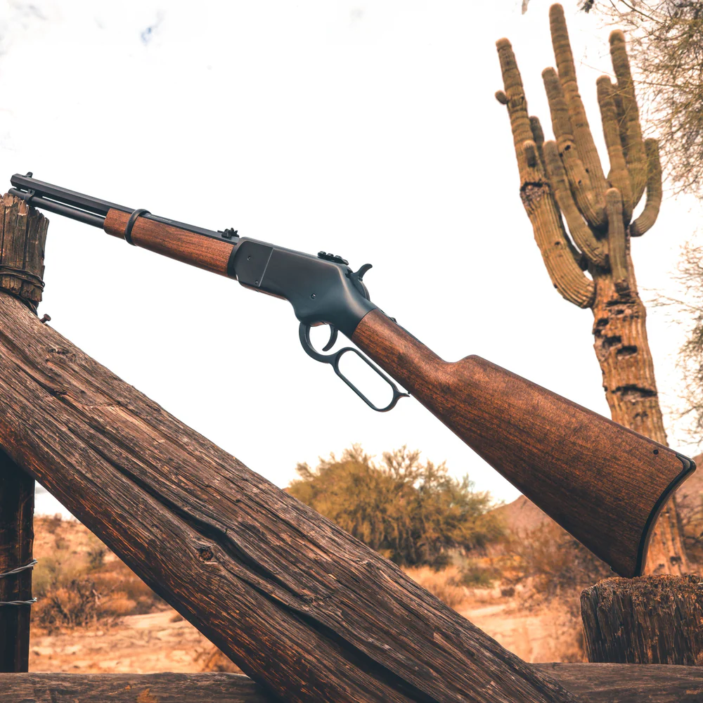 Barra 1866 Lever Action CO2 Air Rifle 5 The Barra 1866 CO2 Lever Action Air Rifle with a wooden stock rests on a weathered fence in a desert landscape, with a tall cactus visible in the background.