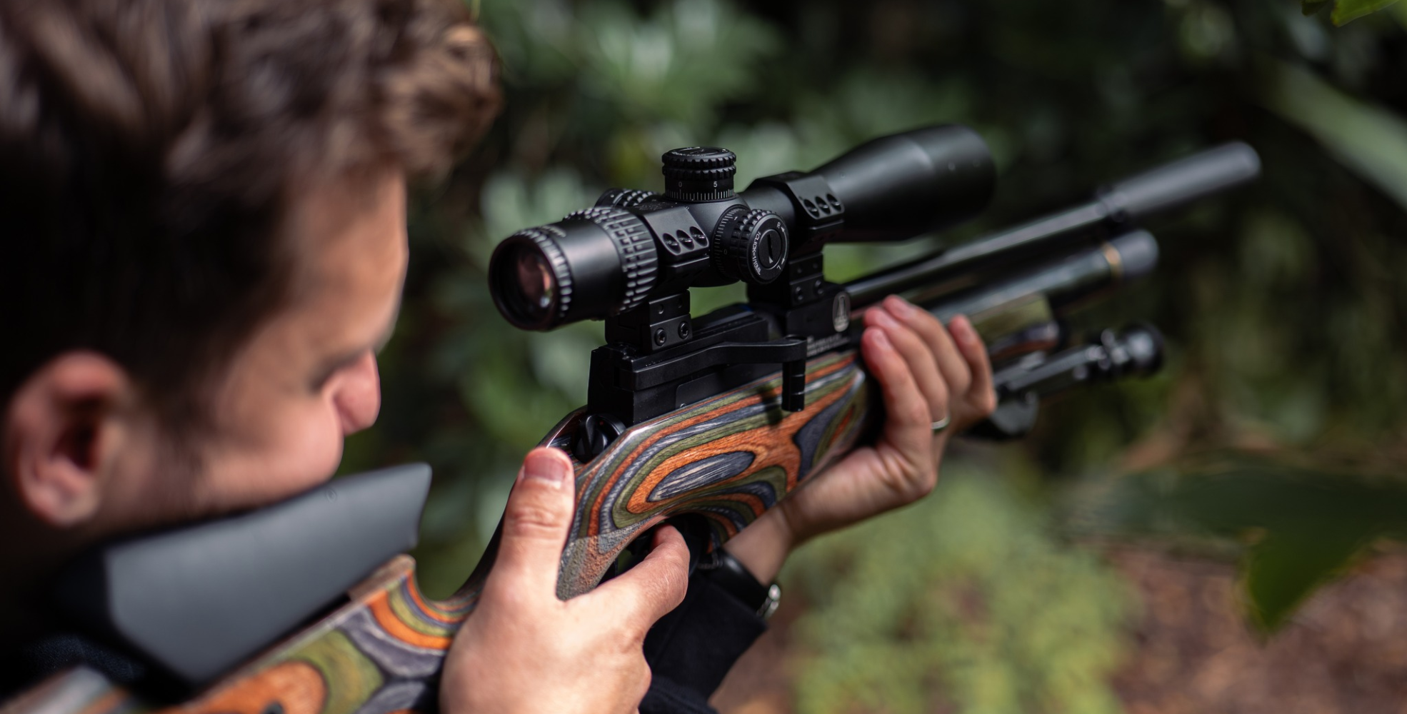 A person aims a scoped rifle outdoors surrounded by greenery, focusing on the rifle and the person's hands&mdash;perfect for those looking to part exchange gun or even Sell your gun in a safe outdoor setting.