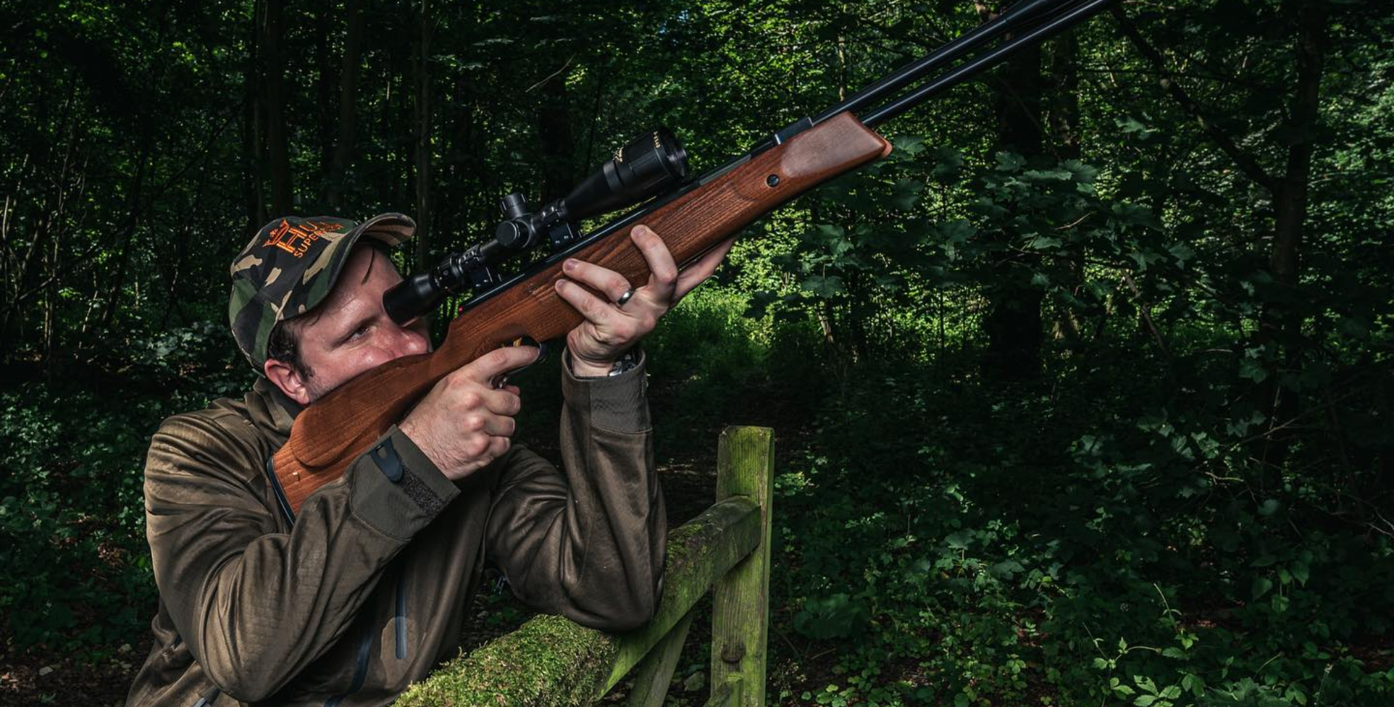 Understanding Weihrauch: A Guide to Model Lettering 1 A person in camouflage clothing aims a scoped Weihrauch air rifle in a wooded outdoor setting, ready to guide their shot with precision.