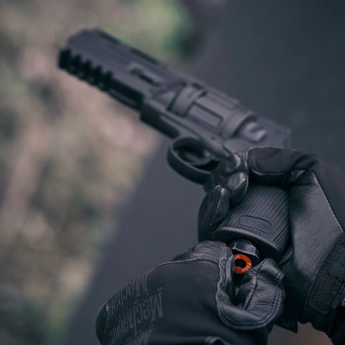 Umarex T4E TR50 HDR 50 Gen2 Paintball Revolver With 50x Paintballs 11 A person wearing black gloves loads an orange-capped CO2 cartridge into the grip of a black Umarex T4E TR 50 Gen 2 CO2 Paintball Revolver With 50x Paintballs.