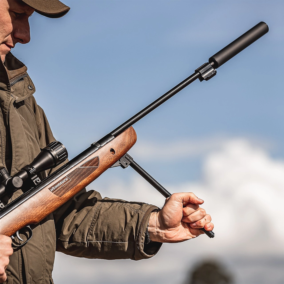 Weihrauch HW57 FTS Spring Air Rifle 5 Person in a brown jacket holding and cocking a Weihrauch HW57 FTS Field Target Sporter Spring Air Rifle outdoors, with blue sky and clouds—ideal for Field Target Sporter competition.