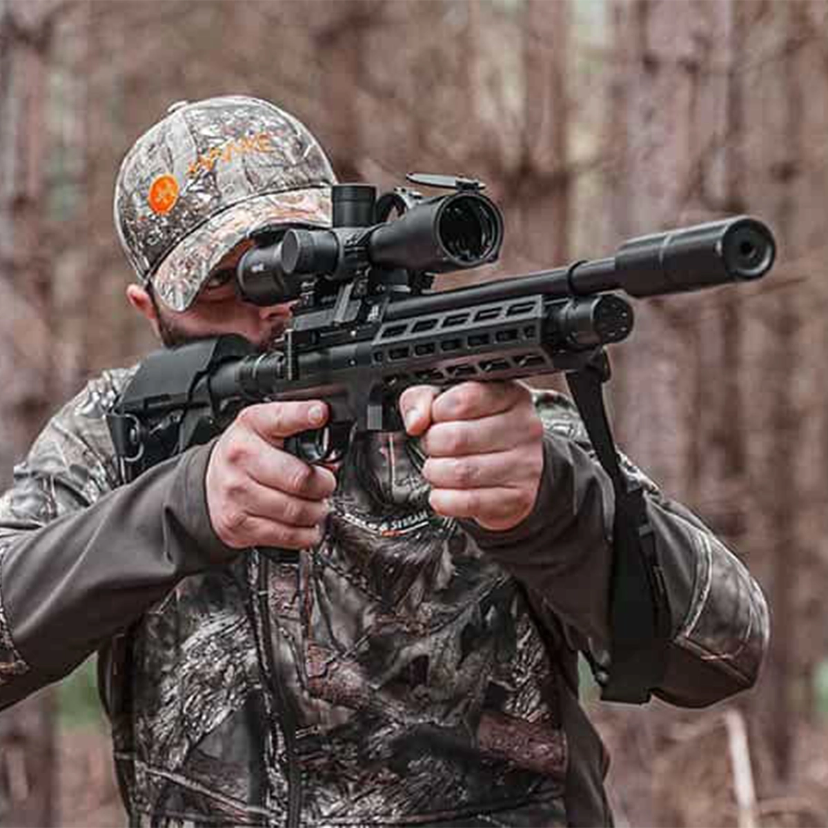 Air Arms S510 Tactical Regulated PCP Air Rifle 11 A person in camouflage clothing aims an Air Arms S510 Tactical Regulated PCP Air Rifle with a scope in a wooded outdoor setting.
