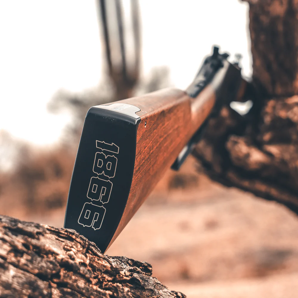 Barra 1866 Lever Action CO2 Air Rifle 7 A close-up of a Barra 1866 Lever Action CO2 Air Rifle resting on a tree branch, with "1866" engraved on the buttstock.