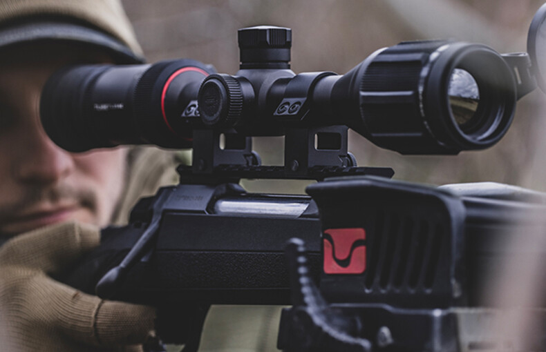 InfiRay TP25 SE Thermal Imaging Rifle Scope With Mounts 5 A person aims a rifle outdoors, focusing through the InfiRay TP25 SE Thermal Imaging Rifle Scope With Mounts, hands steady on the weapon.